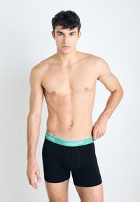 Fekete boxer alsónadrág világoskék derékkal, amelyen a "LACOSTE" logo látható, puha anyagból készült, testhezálló kialakítással.