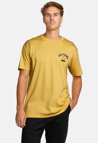 T-shirt giallo senape, in cotone, maniche corte, scollatura rotonda, presenta un logo stampato sul petto sinistro con design a onde.