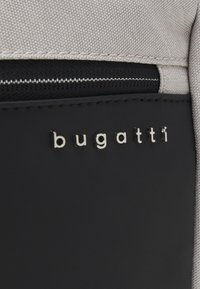 Graue Stofftasche mit einem eleganten schwarzen Panel, akzentuiert mit einem silbernen "bugatti"-Logo und einem Reißverschlussdetail, das eine strukturierte Oberfläche zeigt.