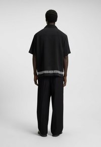 Camicia nera a maniche corte con taglio morbido e bordo decorativo bianco nella parte inferiore. Abbinata a pantaloni neri a gamba larga e scarpe nere.