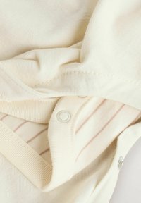 Tissu couleur crème avec une texture douce, présentant un motif rayé et des fermetures à pression le long du bord.