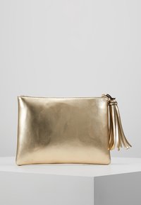 Kultainen keinonahkainen pikkulaukku, jossa on sileä ja kiiltävä pinta sekä vetoketjusuljin. Lisäksi laukun toisella puolella koristeellinen tupsu tuomassa lisäyksityiskohtaa.