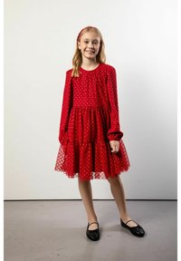 Czerwona sukienka w białe kropki z długimi rękawami, falbanianą spódnicą i siateczkową nakładką. Do tego czarne baleriny i pasująca opaska na głowę.