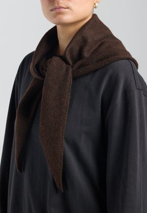 Persoon draagt een donkerbruine wollen sjaal om de hals gebonden over een zwart shirt met lange mouwen, met aan één oor zichtbare oorbellen.