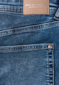 Jeans in denim blu con un'etichetta dettagliata, cuciture a contrasto e un accento in metallo sul taschino.