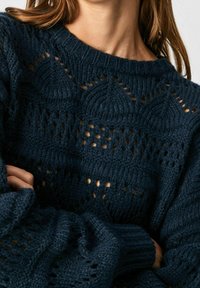 Gebreide trui in donker marineblauw met een gestructureerd, opengewerkt ontwerp met geometrische patronen, een geribde ronde hals en brede mouwen.