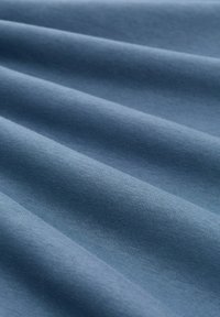 Tekstila audums maigi, bālgani zils tonī ar gludu tekstūru, ar krokām un vienmērīgu izstrādājuma rakstu. Nav redzamu rakstu vai akcentu.