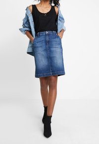 Džínová sukně s vysokým pasem, po kolena, v bledě modré prané barvě. Vytvořena s černým tílkem a džínovou bundou, doplněna kotníkovými botami.