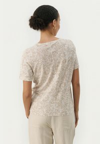Haut à manches courtes beige à fleurs avec une texture légèrement transparente et un col rond, associé à un pantalon léger et ample.