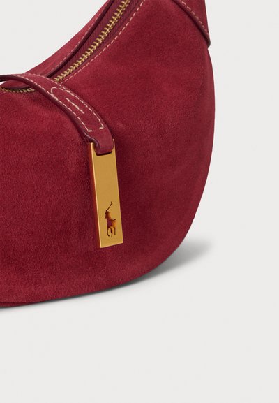 Τσάντα ώμου από σουέντ σε βουργουνδί απόχρωση με στρογγυλεμένο σχήμα, χρυσή ταμπέλα με λογότυπο και αντίθετη ραφή στο λουρί.