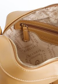 Inuti den bruna läderväskan finns en zipficka och en märkesfabriksinredning med ett upprepat textmönster. Slät yta och subtila sticksömnadsdetaljer.