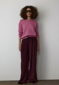 Ružový pletený sveter s okrúhlym výstrihom, skombinovaný so širokými, hlbokými bordovými manšestráckymi nohavicami s šnúrkou v páse a bočnými vreckami.