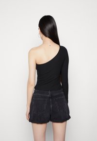 Schwarzes, geripptes Top mit einem Schulterträger, kombiniert mit hochgeschnittenen schwarzen Jeansshorts. Das Top hat eine strukturierte Oberfläche und ein asymmetrisches Design.