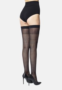 Sorte net strømper der går op til låret med bred topkant, båret med højtaljede sorte shorts og sorte højhælede sko.