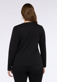 Maglietta nera a maniche lunghe con scollatura tonda, texture liscia e vestibilità comoda, abbinata a jeans scuri. Visualizzata dalla vista posteriore.