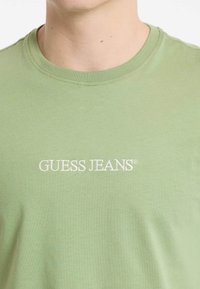 Gaiši zaļš kokvilnas T-krekls ar apaļu kakla izgriezumu. "GUESS JEANS" logo baltā izšuvumā krūtīs. Mīksta tekstūra, ikdienišķs dizains.