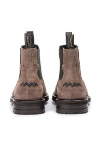 Botas de ante marrón hasta el tobillo con lados elásticos, que presentan un detalle de costura en zigzag en el talón y una suela de goma texturizada.