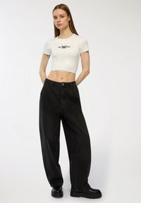 Jeans neri a gamba larga con vita alta e chiusura davanti a bottoni, abbinati a un top corto bianco aderente con una grafica di farfalla.