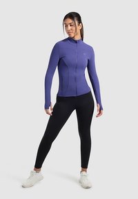 Purple athletic jacket with a full zipper, long sleeves, and side pockets, paired with black leggings and white sneakers.