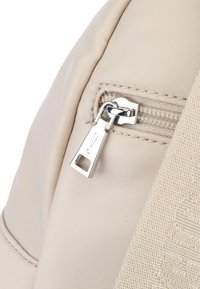 Beige tyg ryggsäck med dragkedja; silverfärgade detaljer och vävd rem med texturerade accenter.