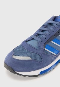 Blue sneaker with a mix of suede and mesh materials, featuring grey accents and three white stripes. Textured surface and rubber sole.