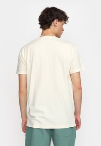 Camiseta corta de manga con cuello redondo en color crema, hecha de un tejido suave, con un diseño liso y un corte relajado, combinada con pantalones cortos de color verde claro.