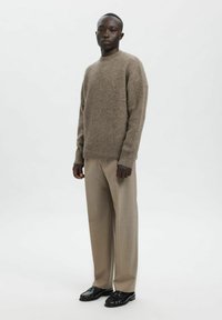 Lysebrun ullgenser med rund hals og ribbestrikkede mansjetter, kombinert med beige vide bukser og svarte loafers. Enkel, teksturert design.