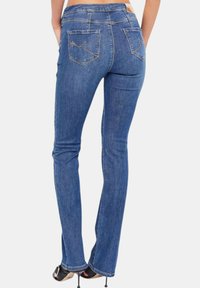 Jeans in denim blu a zampa d'elefante con una texture liscia, tasche posteriori con dettagli di cucitura e vita a media altezza.