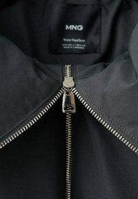 Czarna kurtka odporna na wodę z srebrnym zamkiem błyskawicznym, dużym kołnierzem oraz wewnętrzną metką z napisem "MNG". Gładka tekstura i minimalistyczny design.