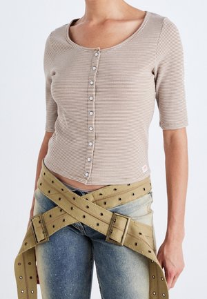 Beżowy prążkowany top z krótkim rękawem, okrągłym dekoltem i guzikami z przodu, w połączeniu z niebieskimi dżinsami i brązowym regulowanym paskiem w stylu uprzęży.
