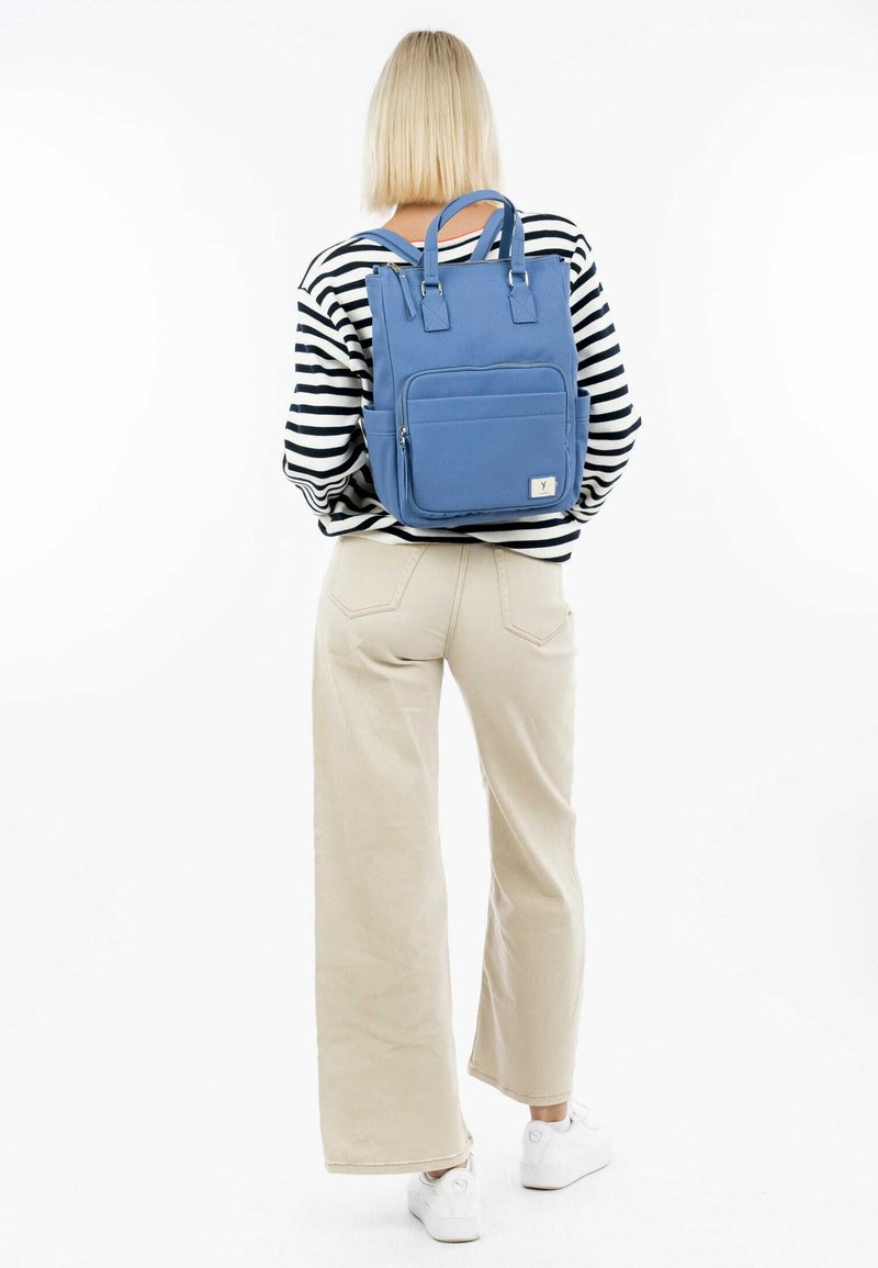 Blue backpack with adjustable straps, front pocket, and top carry handles. Textured fabric, rectangular shape, and white logo tag on the front.
