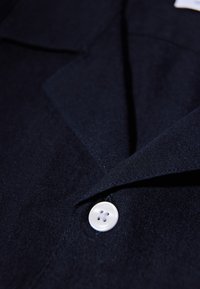 Chemise bleu marine présentant une texture de tissu lisse, un col cranté et un seul bouton blanc à quatre trous.