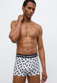 Baltos medžiagos bokseriai su juodu grafiniu piešiniu, elastine juosmens juosta su užrašu „KARL LAGERFELD“ ir aptemu dizainu.