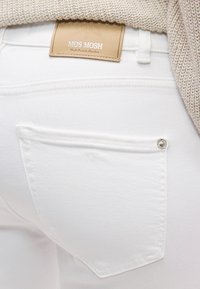 Λευκό τζιν παντελόνι από denim με πίσω τσέπη που διαθέτει ασημί κουμπί, συμπληρωμένο με ετικέτα από μπεζ δέρμα με ανάγλυφο το λογότυπο "MOS MOSH".