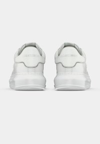 Paire de baskets blanches en cuir vues de dos avec le nom de la marque embossé sur la languette du talon et des semelles épaisses en caoutchouc.