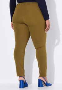 Olivgröna leggings med en slät, stretchig textur, i kombination med blå klackskor. Midjan är elastisk, vilket ger en tät passform.