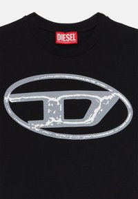 T-shirt en coton noir présentant un grand logo ovale gris avec un "D" stylisé au centre. Étiquette de marque rouge au niveau de l'encolure.