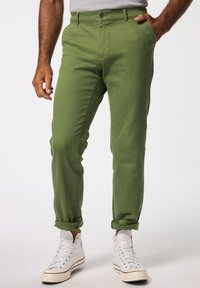 Pantaloni in cotone verde con vestibilità slim, orli arrotolati, tasche frontali e chiusura con bottone standard. Indossati con sneakers alte bianche.