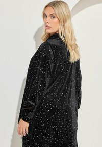 Indumento in velluto nero con motivo a stelle, maniche lunghe e vestibilità ampia. Caratterizzato dalla sua morbida texture e dalla finitura lucida.