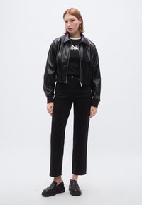 Μαύρο δερμάτινο μπουφάν τύπου μπomber με φερμουάρ μπροστά, φορεμένο πάνω από μαύρο κοντομάνικο μπλουζάκι. Συνδυασμένο με ψηλόμεσα μαύρα τζιν και χοντρά μαύρα παπούτσια.