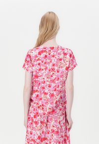 Blusa con motivo floreale in tonalità di rosa, con maniche corte, scollatura rotonda e vestibilità ampia, realizzata in tessuto leggero.
