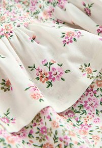 Blumenstoff mit kleinen rosa und orangen Blumen auf einem weißen Hintergrund, mit einem strukturierten Faltenmuster und weichem Baumwollmaterial.
