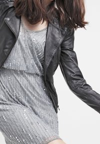 Musta nahkainen moottoripyörätakki hopeasomistetun mekon päällä. Mekko sisältää helmikoristeita ja läpikuultavan päällyksen, sekä kerroksellisen helman.