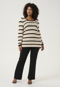 Striped knit sweater in cream and black. Features wide neckline and long sleeves. Pair with black pants and open-toe black heels.
