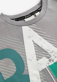 T-shirt in cotone grigio con una grafica audace del numero "4" verde, accenti bianchi invecchiati e sottili linee diagonali sul davanti. Design morbido con collo a giro.