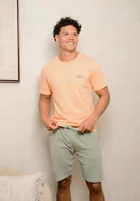 Lichtoranje katoenen t-shirt met een fietsafbeelding; gecombineerd met groene shorts met een elastische taille en trekkoord.
