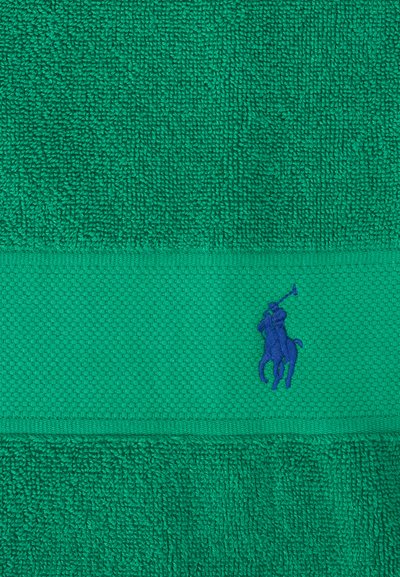 Πράσινη πετσέτα με υφή και οριζόντια ταινία που φέρει μπλε κεντητό λογότυπο παίκτη πόλο πάνω σε άλογο με σηκωμένο το ρόπαλο.