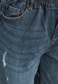 Mörkblå denimjeans med avslappnad passform, elastisk midja, synliga sömmar och slitna detaljer med små revor.