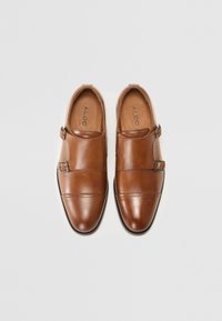 Des chaussures en cuir marron avec une finition lisse, présentant un design à double sangle et des boucles en métal, un bout pointu et des détails de couture subtils.