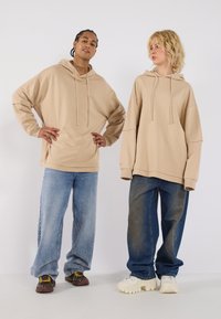 Beige oversized hoodies with drawstrings, paired with loose denim jeans. The footwear includes dark and light sneakers with textured soles.
